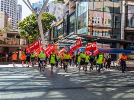A CFMEU protest march in 2019 in Australia with construciton workers waving red CFMEU flags.